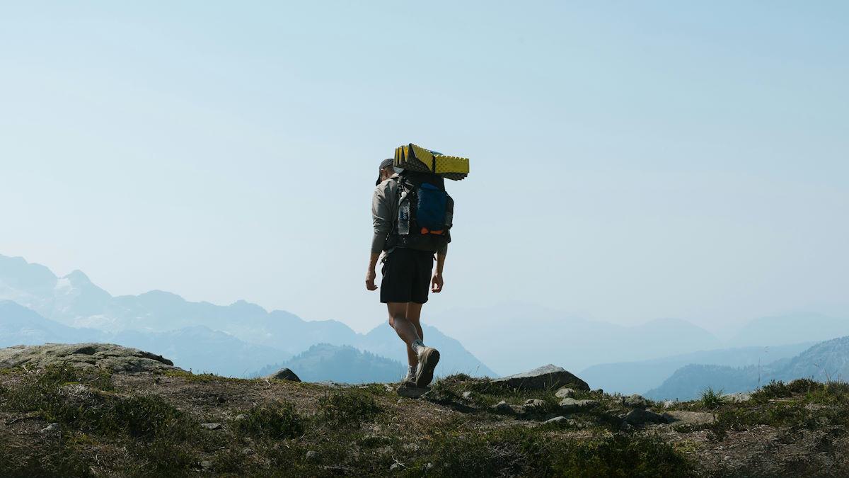 Hiker with backpack on mountain trail in warm evening light